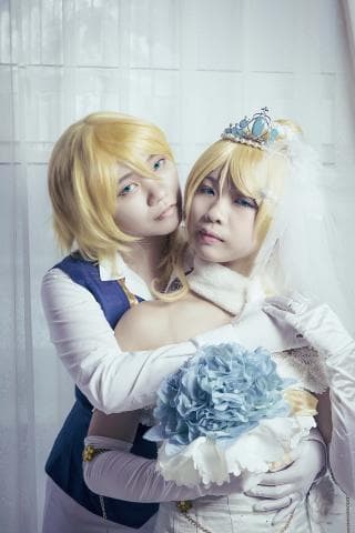 這張「兩個女孩穿著婚紗禮服」的照片是，其中一個女孩穿著正式的白色婚紗禮服，另一個女孩穿著藍色的西裝，她們擁抱在一起，手上拿著花束，看起來很幸福。