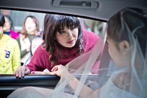 這張照片是一名穿著婚紗的女子，她正坐在汽車的後座，並且微笑著看著鏡頭。她的頭上戴著頭紗，她的笑容很燦爛，讓人感覺到她很幸福。