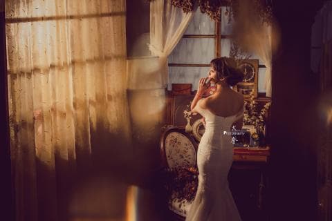 這張「婚紗照」的照片是一個穿著白色婚紗的新娘，站在窗戶前，背景是復古的室內裝潢。