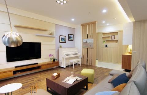 這張照片是一間現代化的客廳，以淺色木質裝潢為主，配上簡約的家具和裝飾，營造出舒適而簡潔的氛圍。照片中，最顯眼的是客廳中央的沙發，以淺色布藝覆蓋，搭配幾顆抱枕，舒適而溫馨。