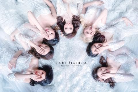 這張「七位穿著白色禮服的女性圍成一圈」的照片是婚紗工作室拍攝的作品，照片中她們的手遮著眼睛，顯得俏皮可愛。