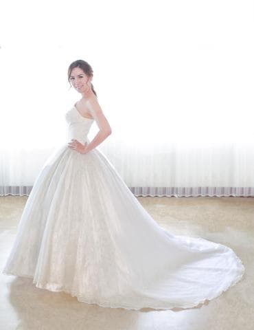 這張照片是一個穿著白色婚紗的新娘，她站在房間裡，對著鏡頭微笑。她穿著一件非常大的婚紗，裙擺拖到地上。