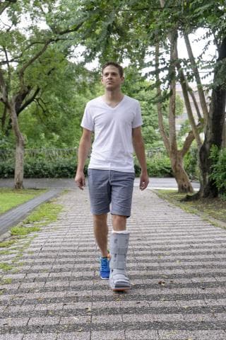 這張「一個男人在石頭路上行走」的照片是一個戴著護腿的男人，他穿著白色T恤和短褲，背景是綠樹。