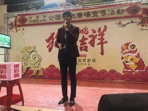 這張「新年活動」的照片是，一名男子站在舞臺上，背景是紅色和金色裝飾，舞臺上有兩隻獅子。