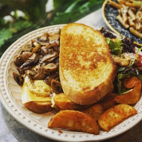 這張「吐司三明治」的照片是 一個烤得金黃酥脆的吐司，夾著炒香菇、起司和炒蛋，配薯條和沙拉。