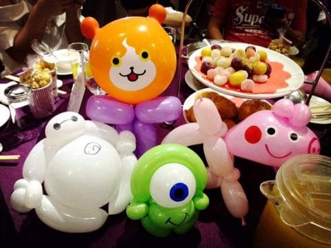 這張照片是一些用氣球做成的可愛角色，其中一個是白色的米奇，另一個是綠色的怪物，還有粉紅色的豬。它們擺放在一張紫色桌布上，顯得十分可愛。