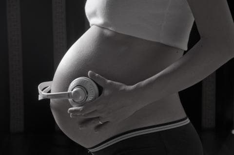 這張照片是一個懷孕的婦女，她把手放在肚子上，頭戴著耳機，似乎在聽音樂。