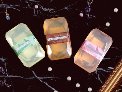 這張照片是三塊不同香味的香皂，其中一塊是綠色包裝的，上面寫著「ORCHID DAIMON」，另一塊是金色包裝的，上面寫著「ORCHID DAIMON」，還有一塊是粉色包裝的，上面寫著「ORCHID DAIMON」。