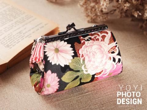 這張「花卉圖案錢包」的照片是一個用黑色布料製成的錢包，上面印著粉紅色和白色的花朵。錢包上還有一個銀色的拉鍊。