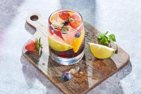 這張照片是一杯用玻璃杯裝著的水果飲品，杯中裝滿了新鮮的草莓、藍莓、葡萄和檸檬，看起來非常清爽可口。