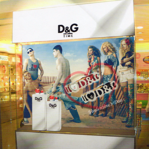 這張照片是一張 D&G 的廣告，照片上展示了四位模特，其中三位是女性，一位是男性，他們身穿 D&G 的服裝，背景是一片沙灘。照片的中心是一個愛心形狀的標誌，上面寫著 "D&G"，下方寫著 "Valentine's Day"。