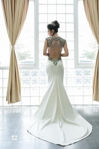 這張照片是一名穿著白色蕾絲婚紗的女性，她的背影展現出優雅的曲線，並帶有一種神秘的氛圍。婚紗的蕾絲設計精美，突顯出女性的柔美，同時也展現出她自信的氣質。