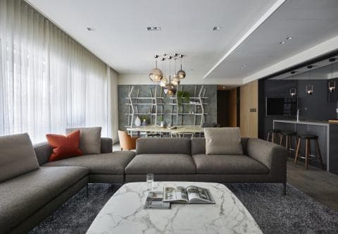這張客廳的照片是一個現代化的空間，佈置著一張灰色的沙發和一張大理石茶几。房間裡還有一盞時尚的吊燈，以及落地窗和窗簾。