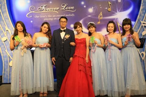 這張婚禮照片是一對新人和他們的伴娘們。新郎穿著西裝，新娘穿著紅色的婚紗，伴娘們都穿著藍色的禮服。