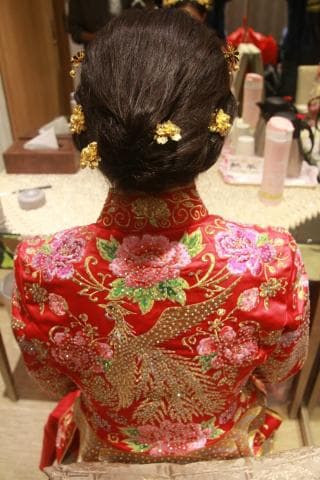 這張照片是一個身穿紅色旗袍的女子，旗袍上繡著精緻的花朵和鳳凰圖案，非常華麗。