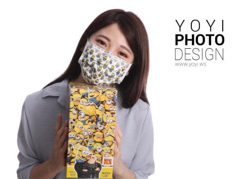 這張照片是一個戴著小黃人圖案口罩的女生，她手裡拿著一盒小黃人圖案的口罩。