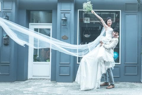 這張照片是一對新人正在進行婚禮拍攝，新郎抱著新娘，新娘的婚紗在空中飄揚，婚紗的紗巾像是一道美麗的彩虹，畫面充滿幸福和浪漫。