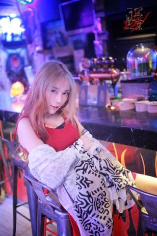 這張「一位穿著紅色洋裝和白色圍巾的女生坐在酒吧裡」的照片是。