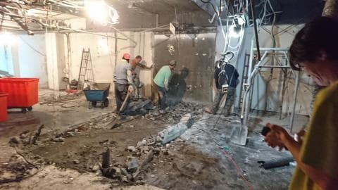 這張照片是一間正在施工的房間，照片的中心是幾位工人正在用工具拆除牆壁和地板。