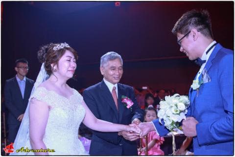 這張照片是一對新人正在交換戒指，他們看起來非常幸福。新郎穿著藍色西裝，新娘穿著白色婚紗，他們的笑容都非常燦爛。