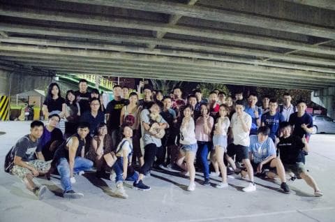 這張「一群人站在橋下」的照片是，一群年輕人站在橋下，看起來很開心，他們可能是在一起聚會或活動。