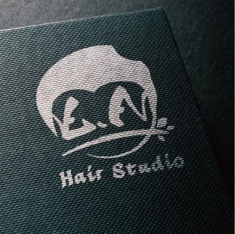 這張照片是一家名為「Hair Studio」的髮廊的標誌，標誌上有一個白色的人形圖案，頭上有一圈像頭髮一樣的圖案，以及「Hair Studio」的文字。