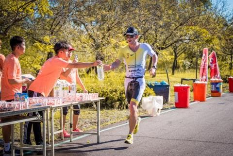 這張照片是一個運動員在比賽中跑過終點線，在終點線上，有工作人員為他遞水。
