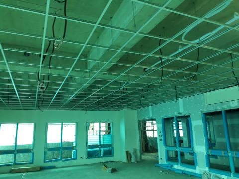 這張照片是一個正在施工的建築空間，最顯眼的是天花板的吊頂，它由許多網格狀的鋁製格柵組成，並配有黑色的電線，預示著不久的將來將會安裝照明設備。