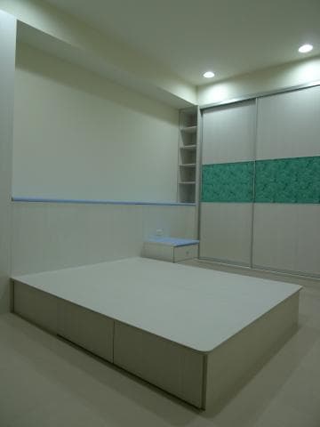 這張照片是一張現代化臥室的照片，房間裡最顯眼的是一個帶有抽屜的白色床架，床架上鋪著白色床墊，床頭櫃上有一個裝飾品。