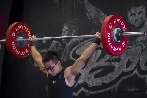 這張照片是一個年輕人正在舉重，他舉起了一個槓鈴，槓鈴上有一個紅色的大重量盤。