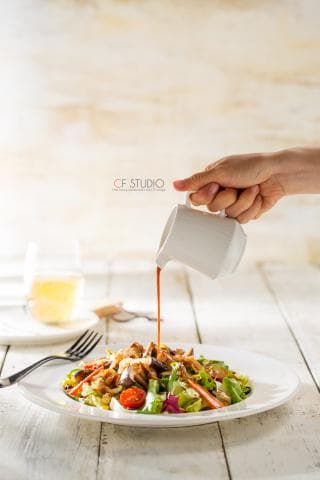 這張「沙拉」的照片是一盤佐以醬汁的沙拉，醬汁正在被倒入沙拉中。