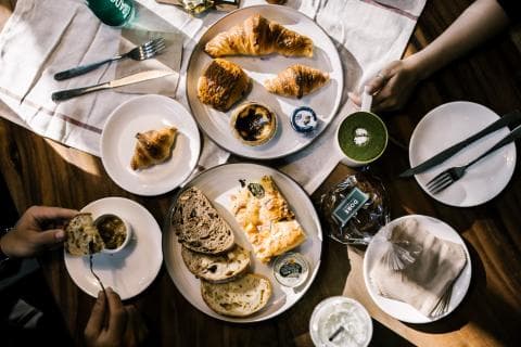 這張「美食」的照片是一張桌子上的食物和飲料，有麵包、糕點、綠茶和咖啡。