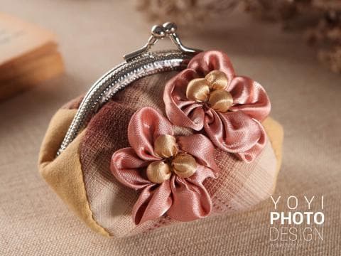 這張照片是一個用粉色緞帶裝飾的錢包。錢包的材質是布料，上面有格紋圖案。錢包上的緞帶做成花朵的形狀，非常漂亮。