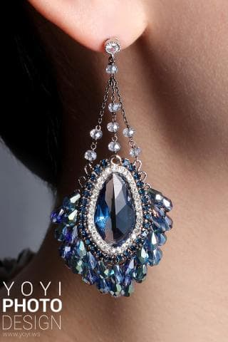 這張照片是一副華麗的耳環，耳環上有許多藍色和白色水晶，形成一朵美麗的花朵。耳環中間有一顆大的藍色水晶，閃閃發光，非常漂亮。