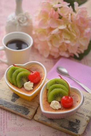 這張照片是兩個裝滿水果和甜點的心形盤子，放在木頭盤子上面，旁邊是一朵粉紅色花。