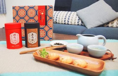 這張照片是一張茶桌，桌上擺著兩罐茶葉、一個茶壺、三個茶杯、一個裝滿餅乾的木盤，以及一個裝滿茶葉的罐子。