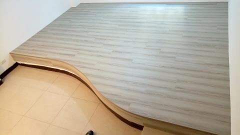 這張照片是一個有弧形邊緣的木地板平台。地板呈淺灰色，上面有仿木紋理。平台邊緣用木條和棕色條裝飾，讓它更美觀。