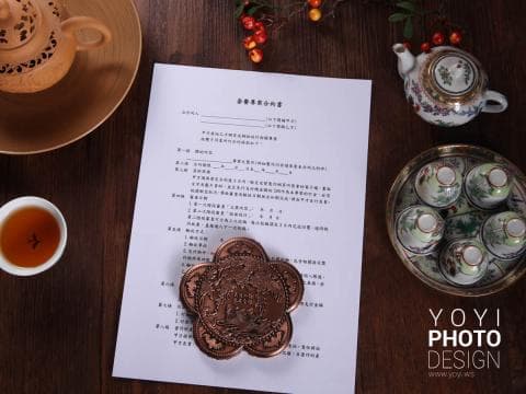 這張照片是一張中式合約，上面印有繁體中文。合約的旁邊是一張精緻的茶托，上面放著一個雕刻精美的銅製茶墊。