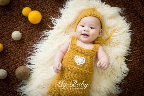 這張照片是一個可愛的嬰兒，穿著黃色的毛衣和褲子，躺在白色毛毯上，他笑得很開心，看起來很可愛。