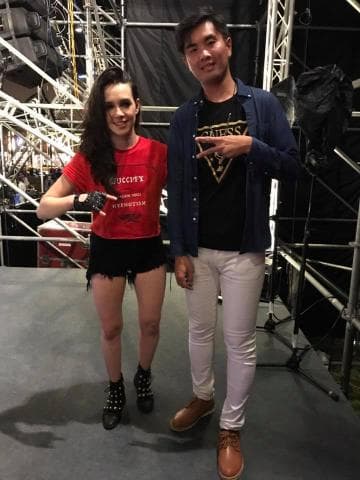 這張照片是一對男女站在一起，他們看起來很開心，他們都穿著很時尚的衣服，女生穿著紅色上衣，男生穿著深藍色外套和白色褲子，他們站在一個看起來像舞臺的背景前。