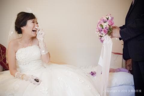 這張照片是一個婚禮的畫面，新娘穿著婚紗，露出開心的笑容，而新郎則站在一旁，手拿著捧花。