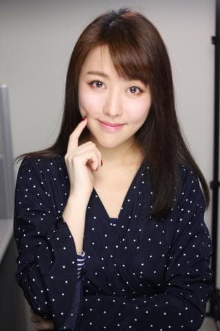 這張照片是一個年輕女性，她穿著一件藍色帶白色圓點的洋裝，她的頭髮是深棕色，她正在微笑。