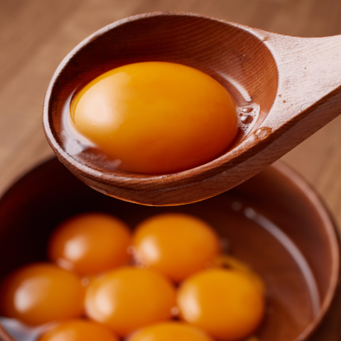 這張照片是一碗蛋黃，其中一個蛋黃被木勺舀起，蛋黃呈現出金黃色的光澤。