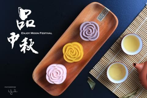 這張「中秋節」的照片是三個不同顏色的月餅，放在木盤上，旁邊放了兩杯茶。