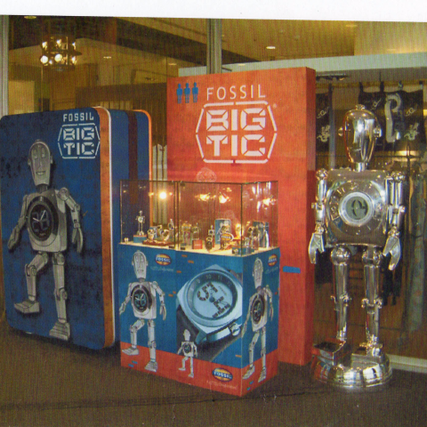 這張照片是一家名為「FOSSIL」的鐘錶品牌的櫥窗展示。櫥窗的中心放置了一臺巨大的機器人，機器人身上裝飾著一個巨大的鐘錶，這突顯了「FOSSIL」品牌的特色。