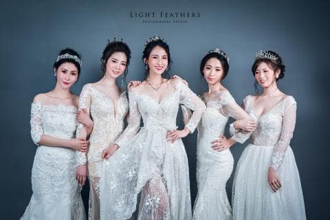 這張「五位穿著婚紗的女性」的照片，其中一位站在中間，她的婚紗比較特別，其他四位則穿著較為傳統的婚紗。她們都戴著皇冠，看起來像是參加婚禮或宴會。