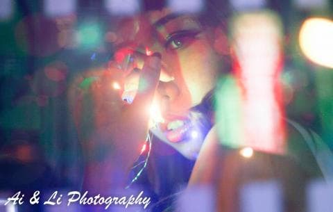 這張照片是一名女性在燈光下用手遮擋眼睛，她的臉被燈光照亮，看起來很神秘。