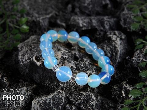 這張「手鍊」的照片是一條藍色水晶珠手鍊，放在岩石上。