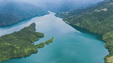這張「山間湖泊」的照片是從高空俯瞰一個被綠色山脈環繞的湖泊。湖泊水色清澈，形狀蜿蜒曲折，岸邊是茂密的樹林，呈現出一幅美麗的自然景色。