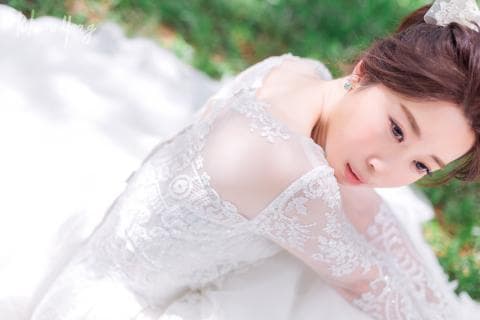 這張照片是一個穿著白色蕾絲婚紗的女孩，她低頭看著地面，展現出優雅而柔美的氣質。婚紗上的蕾絲花紋十分精緻，更增添了浪漫氛圍。